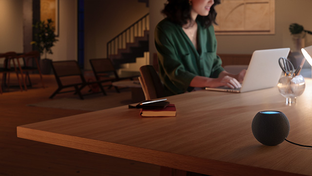 Une pièce éclairée avec une table en bois où se trouvent un ordinateur portable, un Enceinte bleu et des accessoires.