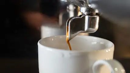 Espresso stroomt uit een metalen machine in een witte mok. De achtergrond is donker.