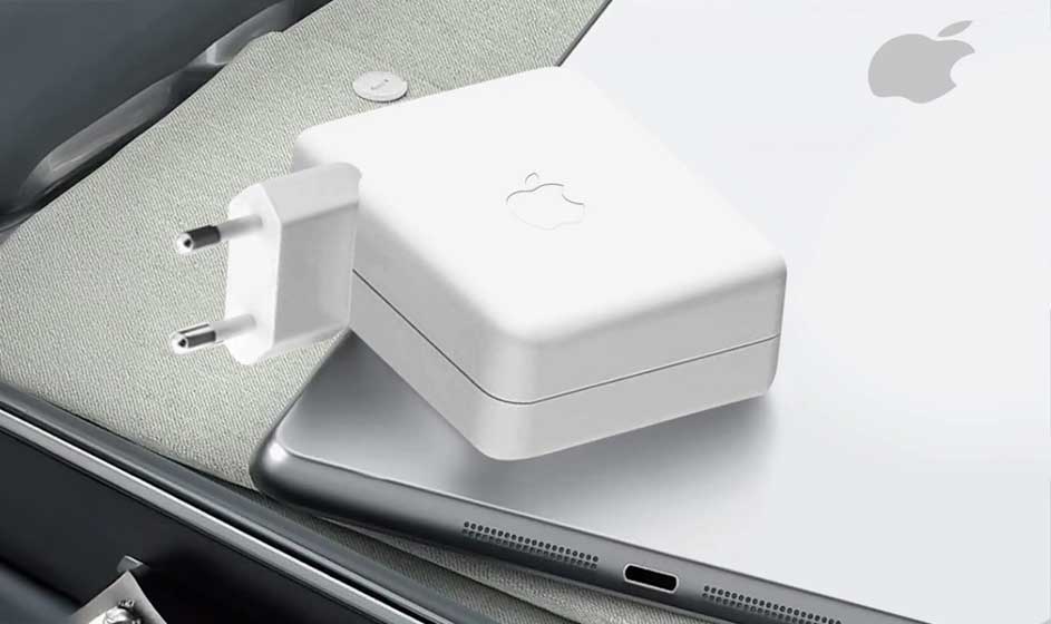 Een witte Apple-oplader ligt op een zilverkleurige laptop naast een tablet. De stekker en kabelaansluiting zijn duidelijk zichtbaar.