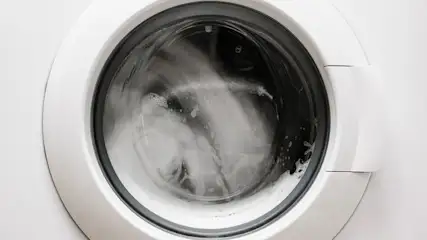 Vue rapprochée d'un lave-linge blanc en marche, avec du linge et de la mousse visibles à travers le hublot.