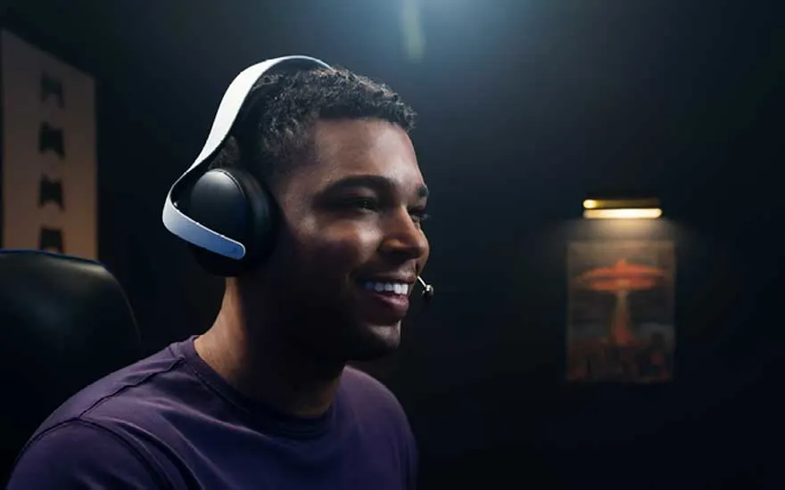 Een gamer draagt een wit gaming-headset met microfoon en glimlacht, zittend in een donkere gaming-omgeving met sfeervolle verlichting en gele accenten op de achtergrond.