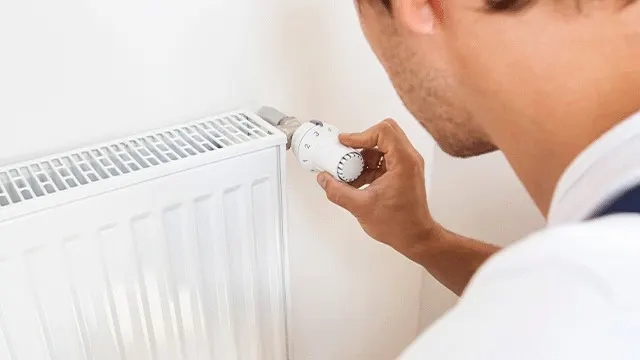 Een witte radiator hangt aan een witte muur, met een hand die de witte thermostaatknop aanpast.