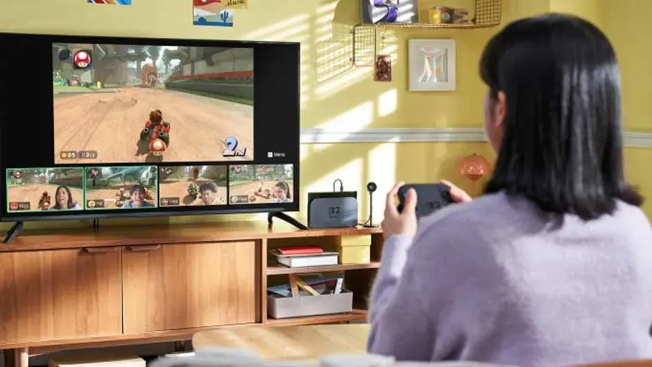 Une télévision affiche un jeu vidéo de course avec des vues des joueurs en bas. Une console de jeu est visible sur un meuble en bois.