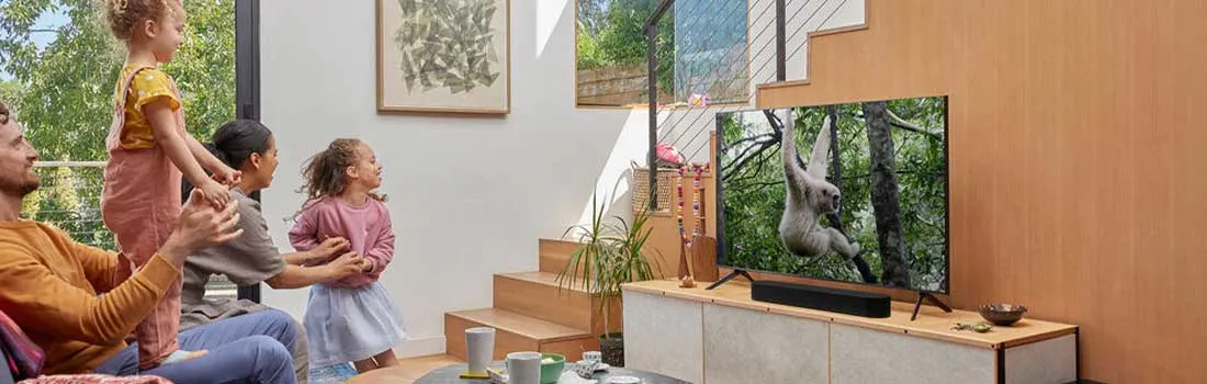 Une famille joyeuse regarde un programme animalier à la télévision dans un salon lumineux avec escalier en bois et déco moderne.