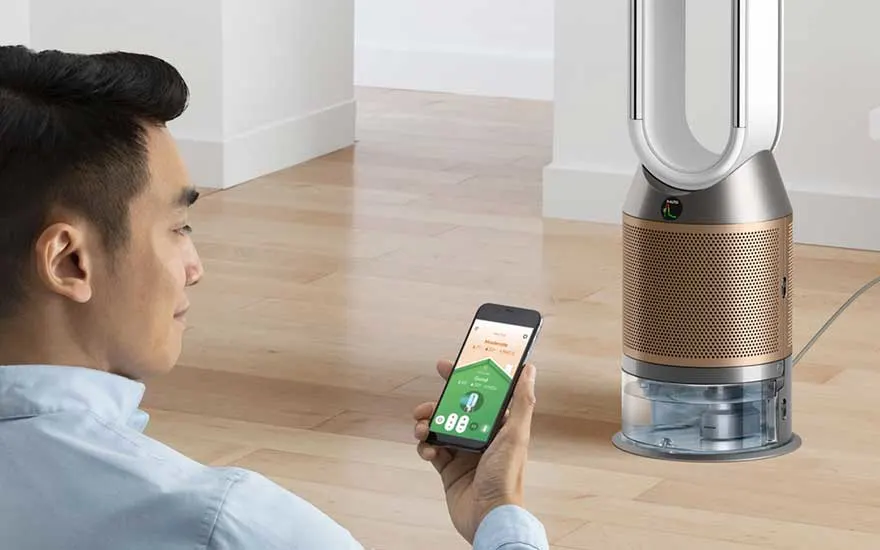 Een man bedient via zijn smartphone een slimme Dyson-luchtreiniger en ventilator die op een houten vloer in huis staat.