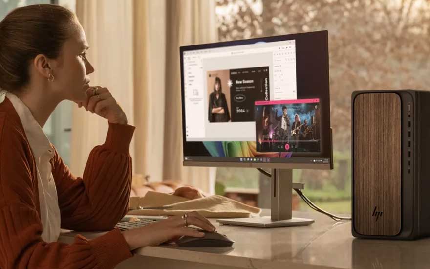 Een vrouw werkt geconcentreerd aan een desktopcomputer waarop een ontwerp en een video zichtbaar zijn, met een stijlvolle pc naast het scherm.