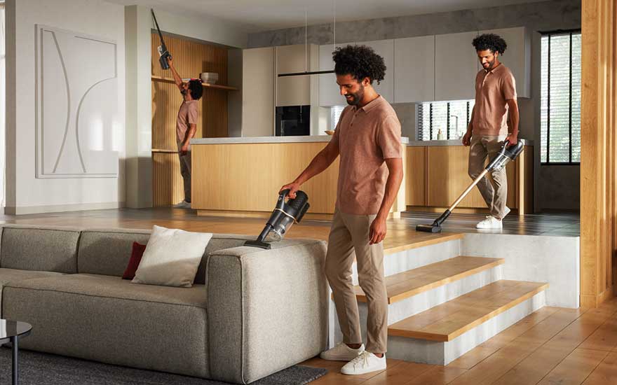 Intérieur moderne avec canapé gris, escaliers en bois et cuisine ouverte. Aspirateurs utilisés sur diverses surfaces.