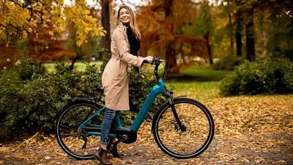Une bicyclette turquoise sur un chemin jonché de feuilles d'automne, avec des arbres aux couleurs automnales en arrière-plan.