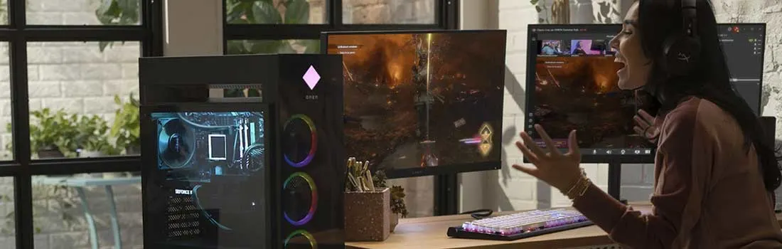 A computer setup featuring a monitor displaying a game, a desktop computer, keyboard, and mouse on a desk.