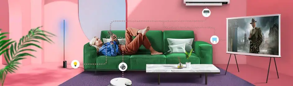 Salon rose avec canapé vert, table basse et télévision. Un aspirateur robotique se trouve sur un tapis violet.