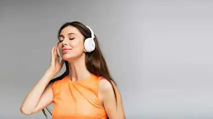 Een vrouw met een oranje top en witte koptelefoon tegen een grijze achtergrond.