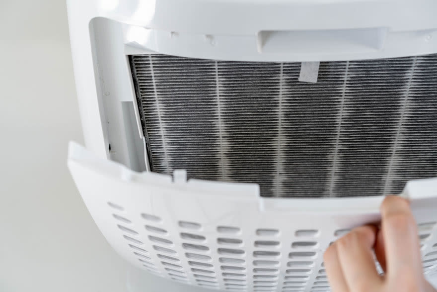 Een close-up van een witte ontvochtiger met een zichtbaar, stoffig filter achter een verwijderde plastic kap.