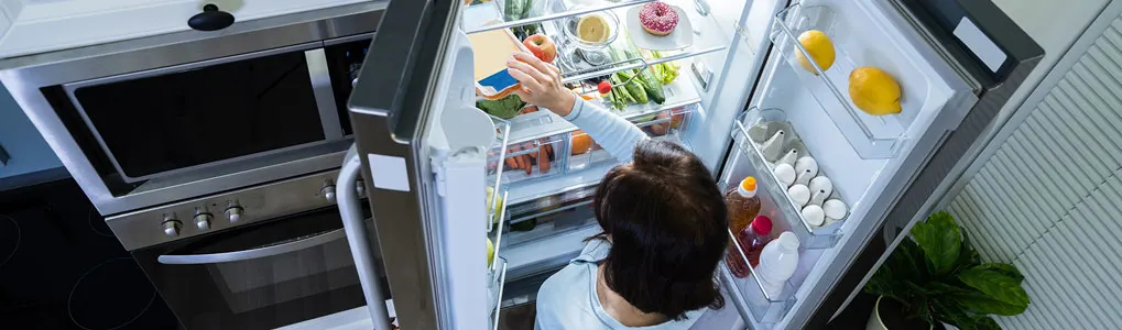 Vue plongeante d'un réfrigérateur ouvert rempli de nourriture, à côté d'un four en acier inoxydable.