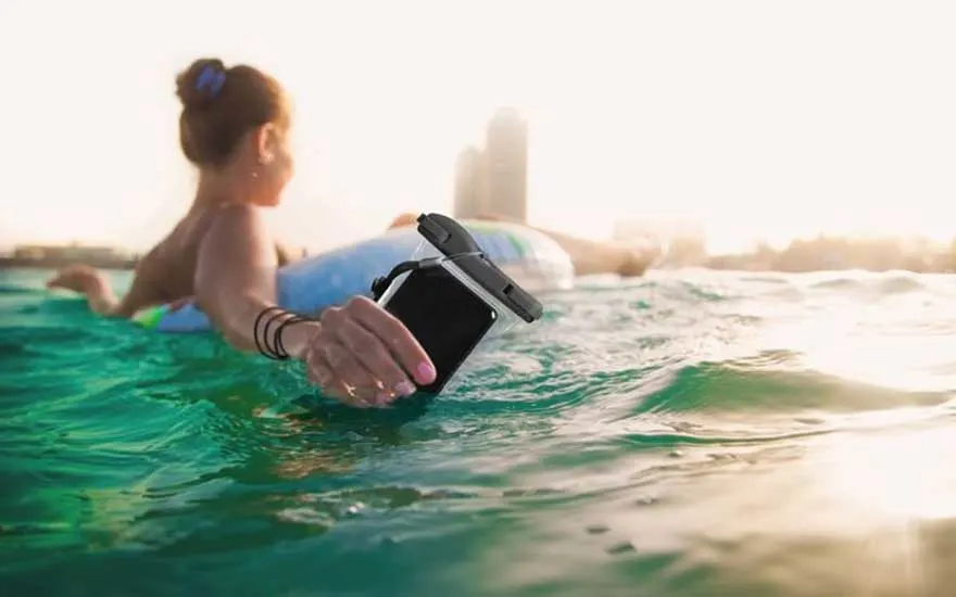 Een persoon dobbert op een opblaasband in het water en houdt een smartphone in een waterdichte hoes stevig vast.
