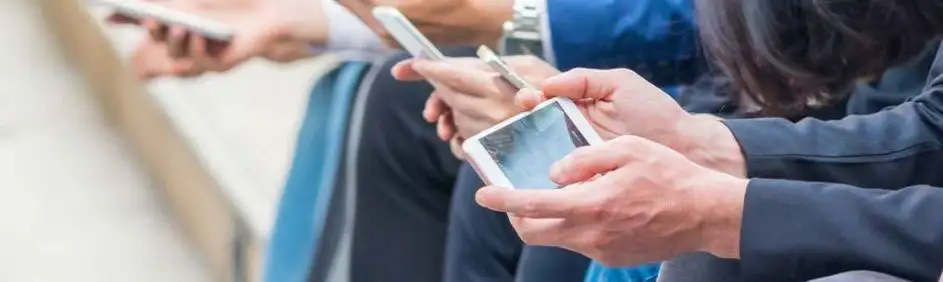 Close-up of hands holding smartphones. The devices are white and reflect light, suggesting a digital interface.