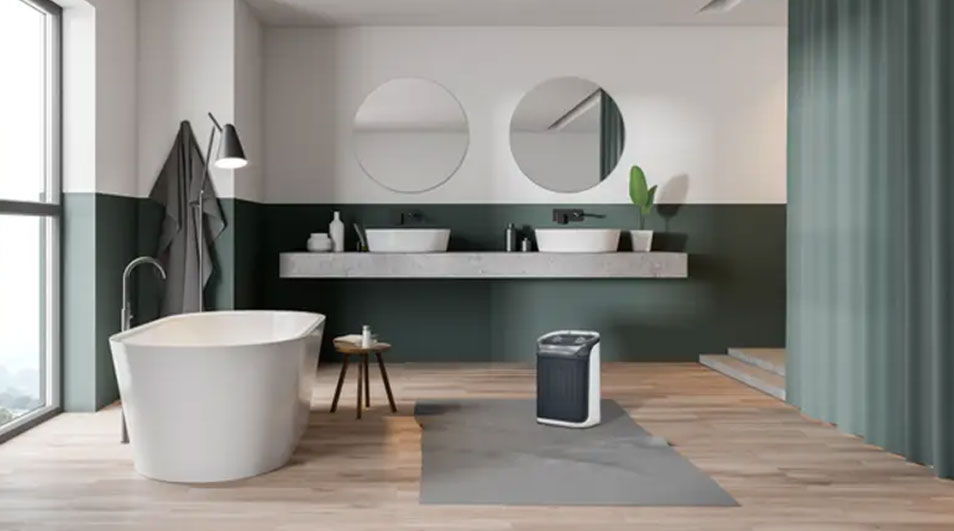 Een badkamer met een wit bad, houten vloer, twee ronde spiegels en een grijs-groene wand.