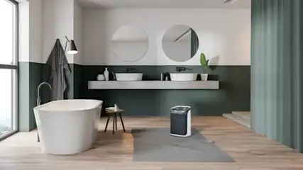 Een badkamer met een wit bad, houten vloer, twee ronde spiegels en een grijs-groene wand.