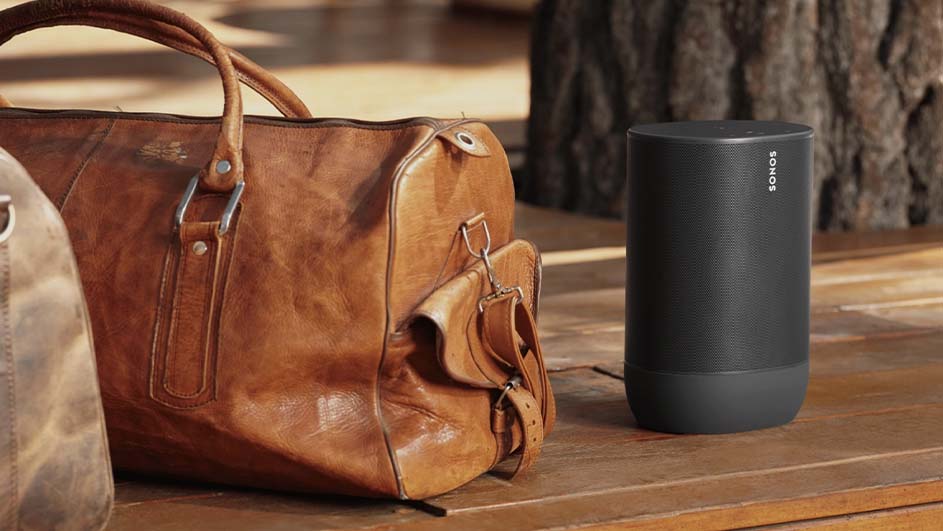 Un sac de voyage en cuir marron est à côté d'un haut-parleur noir Sonos sur une surface en bois.