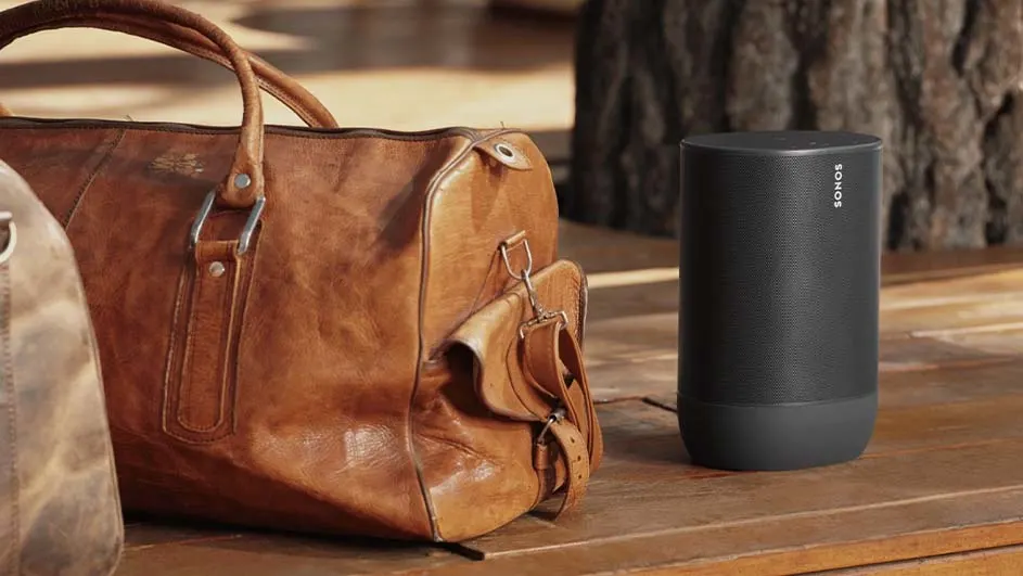 Un sac de voyage en cuir marron est à côté d'un haut-parleur noir Sonos sur une surface en bois.