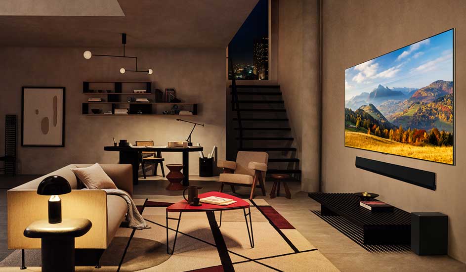 Salon moderne avec canapé beige, table rouge, téléviseur affichant un paysage montagneux, et escalier.