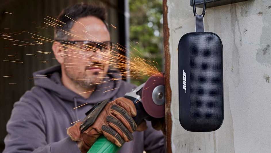 Een slijpmachine in actie, vonken vliegen. Naast de werkplek hangt een zwarte Bose-luidspreker aan de muur.