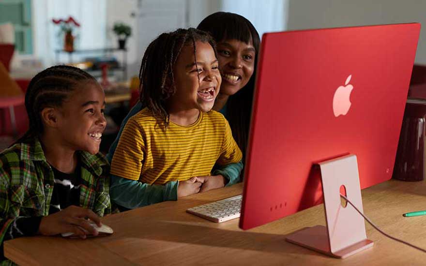 Trois personnes devant un ordinateur rouge avec un clavier blanc sur une table en bois.