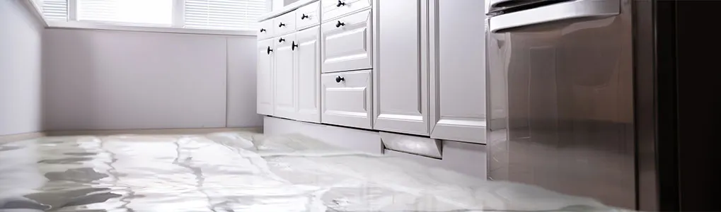 Vue d'une cuisine avec des armoires blanches et un sol inondé, près d'un réfrigérateur en acier inoxydable.