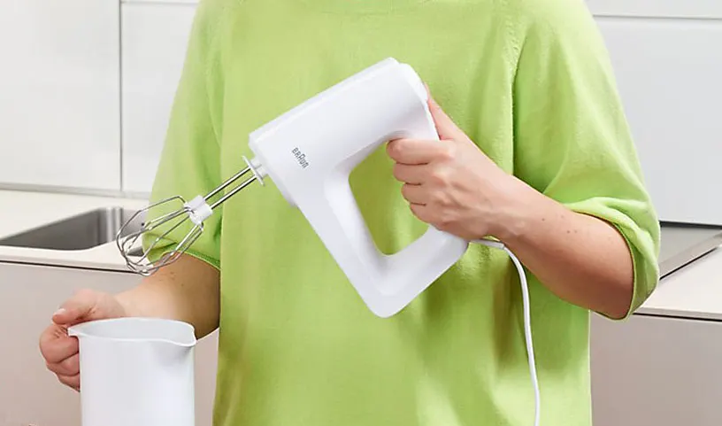 Une cuisine avec un batteur blanc au-dessus d'un pichet, sur fond blanc.