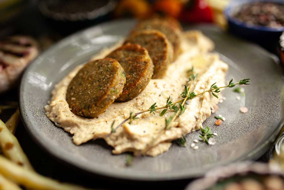 Quatre galettes vertes sur une purée beige, décorées de thym, dans une assiette grise.