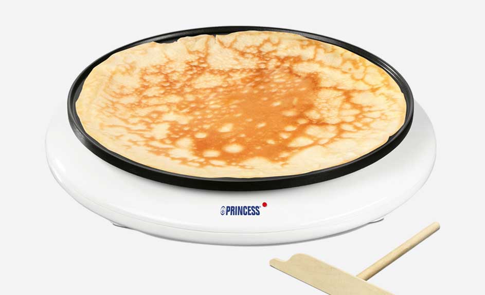 Machine à crêpes blanche avec une crêpe dorée en cuisson. Une spatule en bois est visible.