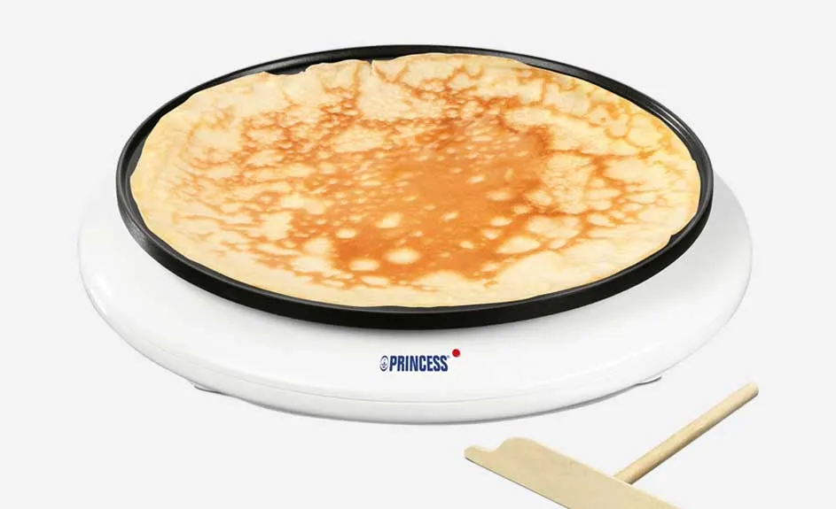 Machine à crêpes blanche avec une crêpe dorée en cuisson. Une spatule en bois est visible.