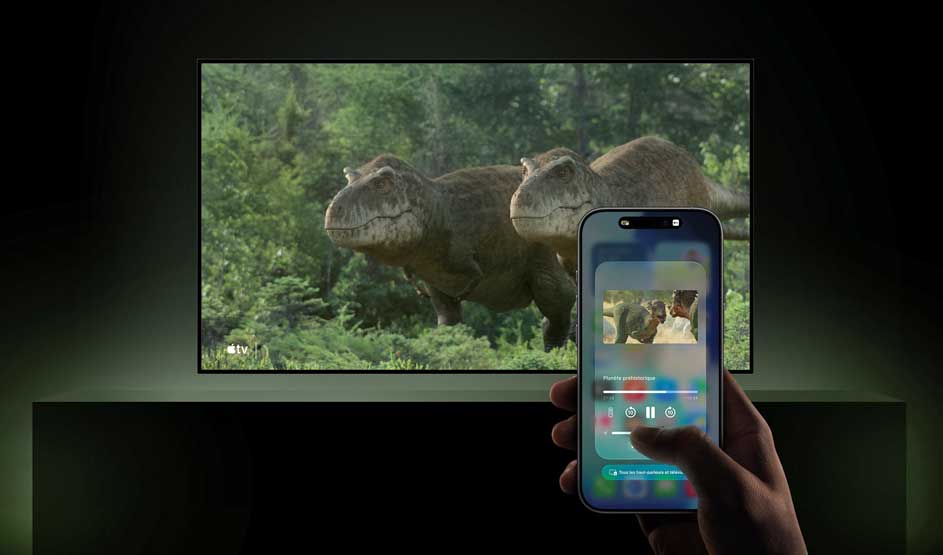 Des dinosaures apparaissent sur un grand écran dans une forêt, tandis qu’une personne contrôle le média avec un smartphone.