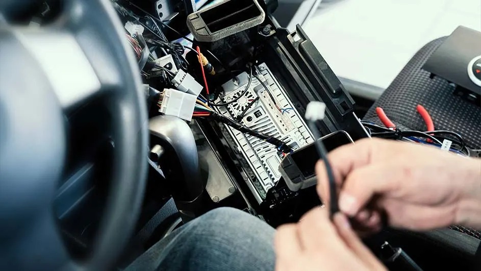 Interieur van een auto met blootliggende bedrading en een dashboard in reparatie, focus op elektronica en kabels.