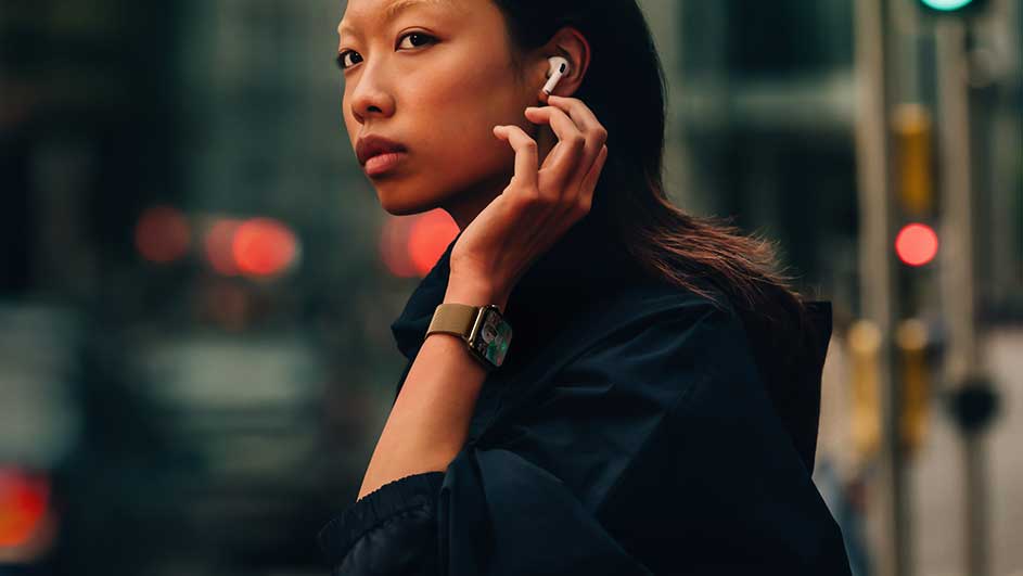 Een close-up van een horloge met een beige band, een witte oortelefoon en lichtreclame op een donkere achtergrond.