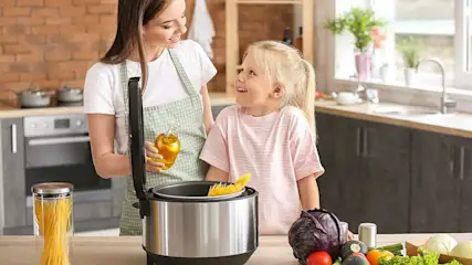 Une cuisine avec une marmite en acier, des légumes et des pâtes sur une table. Huile dans une bouteille en verre.