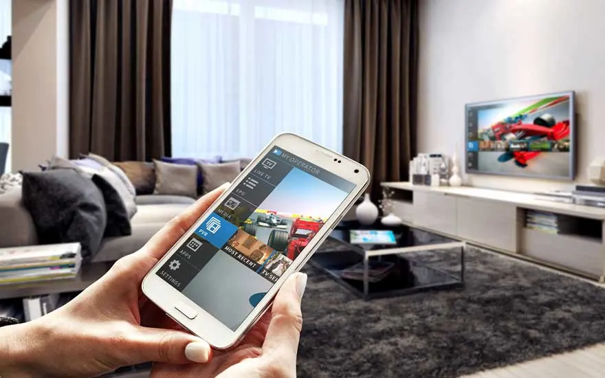 Een witte smartphone met een app-interface wordt vastgehouden in een woonkamer met een tv, sofa, en gordijnen.