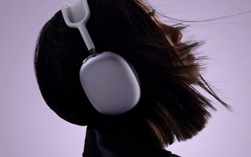 Profiel van een persoon met donker haar dat naar achter waait, draag een lichtpaarse hoofdtelefoon tegen een zachte lila achtergrond, ogen half gesloten.