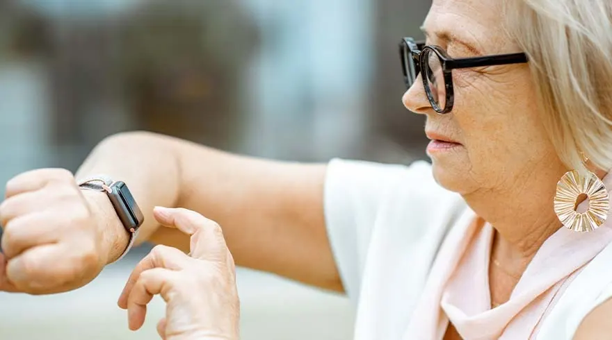Une montre intelligente noire est au poignet. Une main touche l'écran. L'arrière-plan est flou.