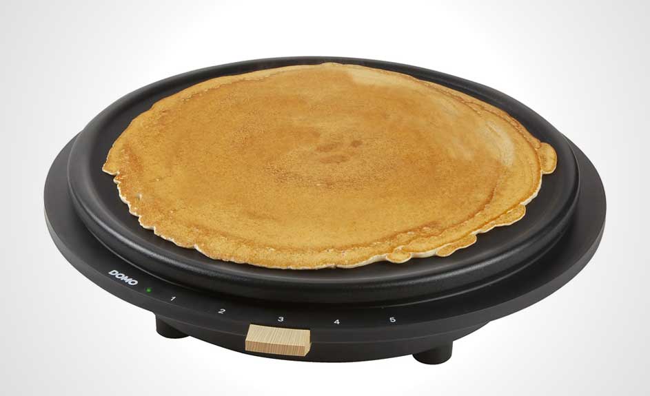 Crêpe dorée sur une crêpière noire. La crêpière a un bouton en bois clair et des réglages de température numérotés.