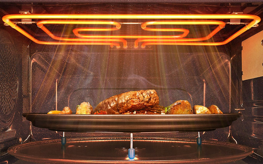 Een oven met een gloeiend verwarmingselement erboven. Op een zwarte schaal ligt gebraden vlees en aardappelen.