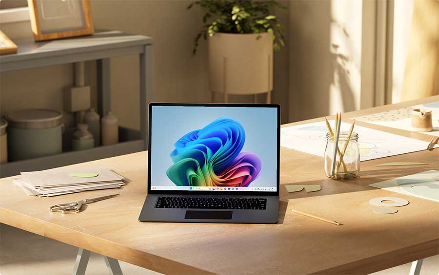 Een grijze laptop staat open op een houten bureau met kantoorartikelen en planten op de achtergrond.