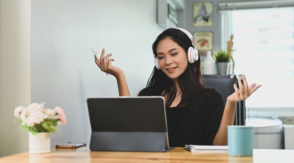 Een laptop op een houten bureau, met een blauwe beker, bloemen en een telefoon, tegen een witte achtergrond.