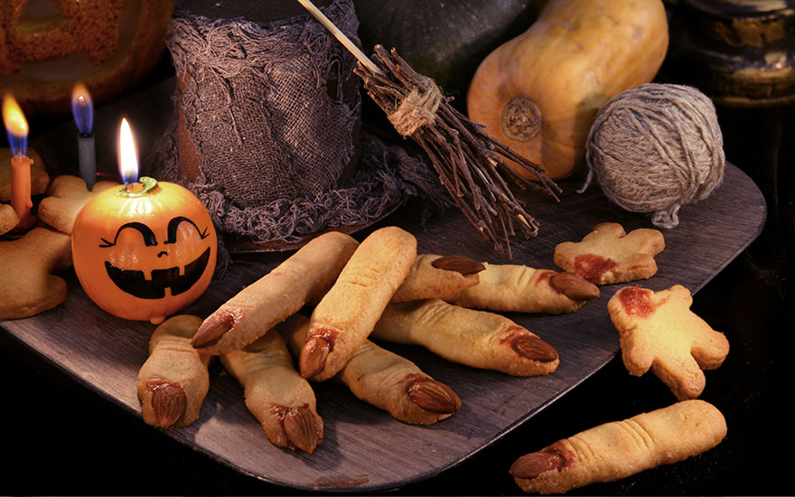 Nature morte d'Halloween avec des biscuits en forme de doigts et de citrouille. Chandelles allumées et balai décoratif.