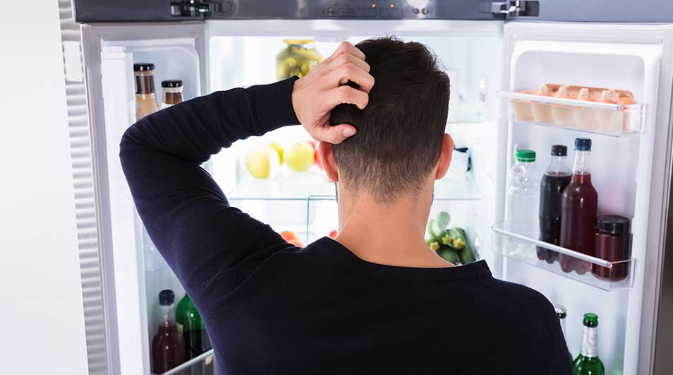Un frigo blanc ouvert révèle des fruits, des légumes et des bouteilles sur ses étagères éclairées.
