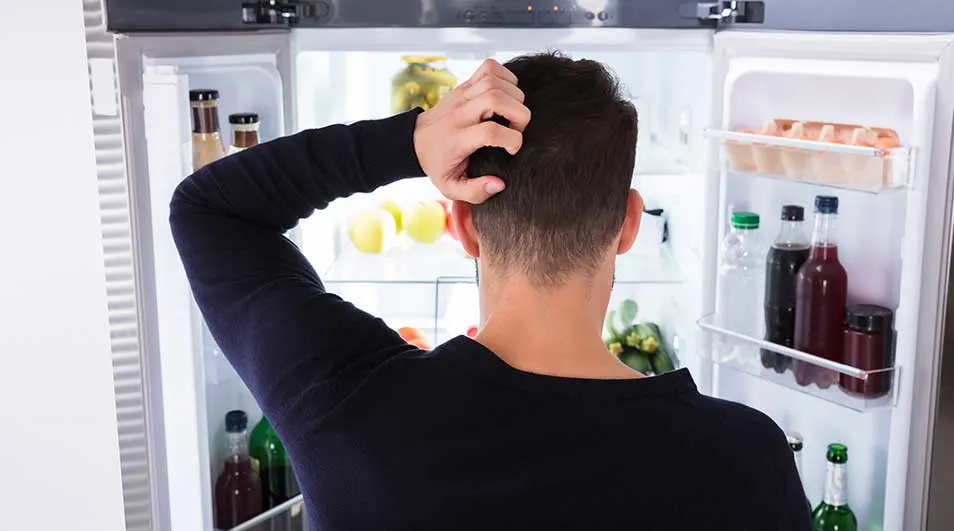 Un frigo blanc ouvert révèle des fruits, des légumes et des bouteilles sur ses étagères éclairées.