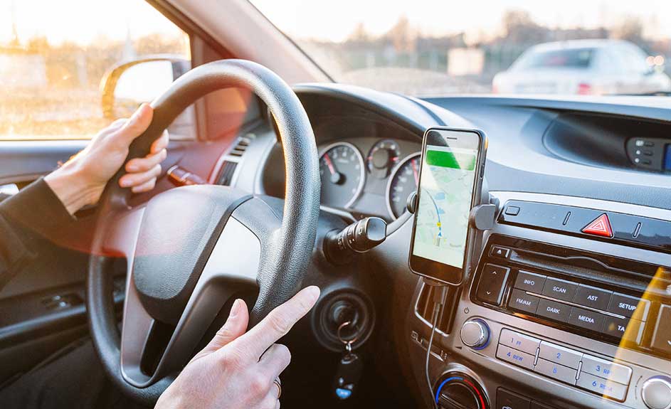 Intérieur d'une voiture avec un téléphone affichant une carte GPS. Le volant et le tableau de bord sont gris et noirs.