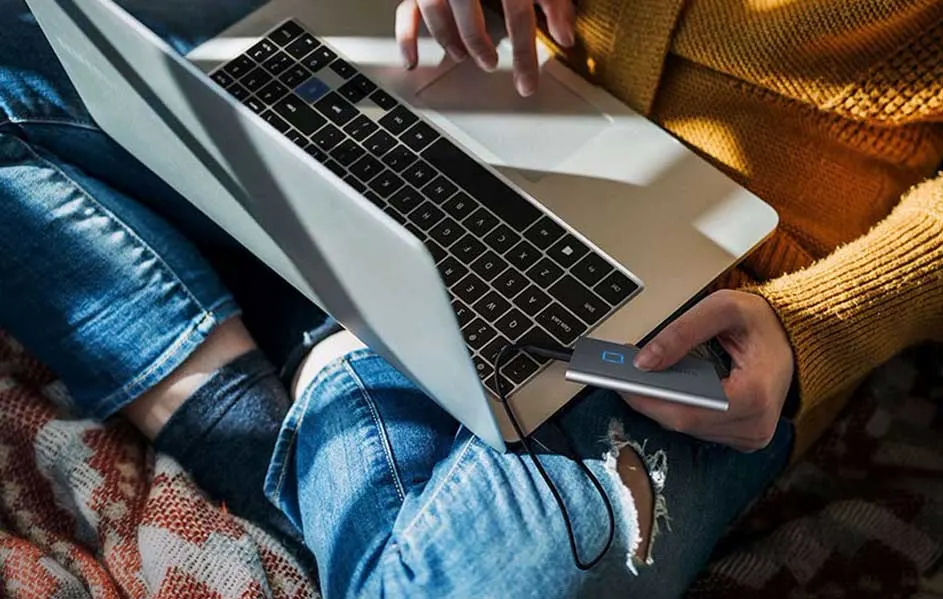 Een laptop op schoot met een externe harde schijf aangesloten, zittend op een deken.