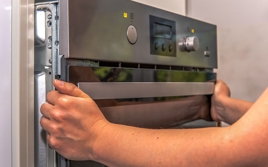 Une main ouvre la porte d'un four en acier inoxydable avec écran et boutons.