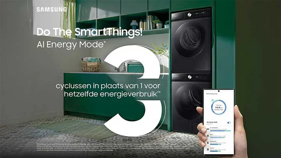 Zwarte wasmachine en droogkast staan in een kamer met groene kasten. Een hand houdt een telefoon vast.