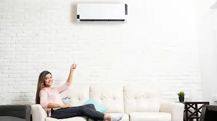Een witte woonkamer met een witte bakstenen muur en een airconditioner. Een witte bank staat tegen de muur.